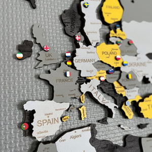 Flag pins added to a GeoArte wooden world map to mark visited countries and future trips.